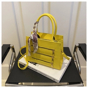 Detail of yellow tote bag with three zippers and a decorative printed silk scarf on the handle