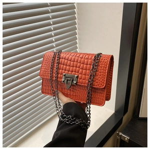 Detail of coral orange crocodile-patterned bag with gunmetal twist lock and studs