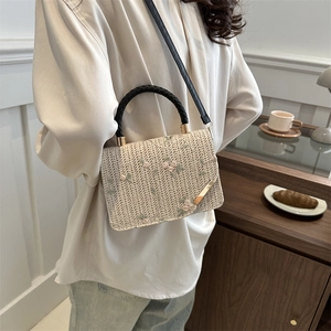 Sac à main tissé beige avec broderie florale et anses noires porté par un mannequin
