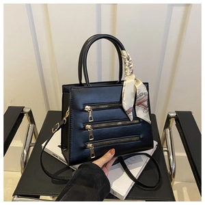 Detail of a black leather tote bag with gold zippers and a silk scarf on a black chair