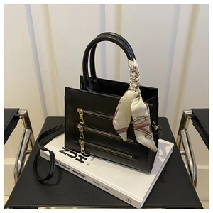Detail of black faux leather handbag with gold zippers and silk scarf on white books