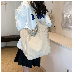 Large beige tote bag with textured fabric shown on shoulder in a lifestyle setting