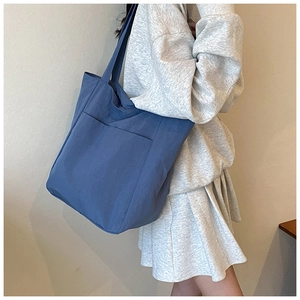 Blue canvas tote bag with dual front pockets shown worn by a model in casual setting