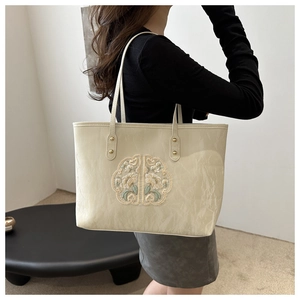 Close-up of beige tote bag featuring elegant floral embroidery and natural pleated texture
