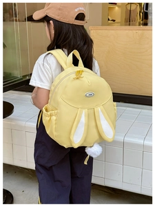 Detail of yellow rabbit ears backpack with plush tail on young model in soft indoor light
