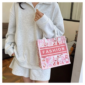Détail d'un cabas en toile rose à motifs floraux et texte Fashion tenu par un mannequin