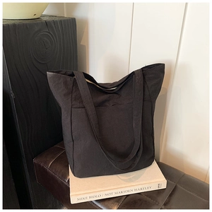 Close-up of a black canvas tote bag with front pocket resting on books in a cozy setting
