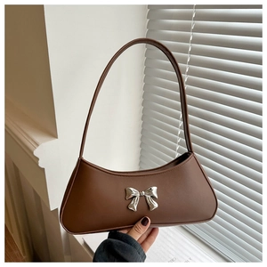 Close-up of a brown baguette bag featuring a silver metal bow and matte leather texture