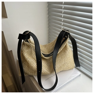 Fashionable beige woven straw crossbody bag with black leather strap on window ledge