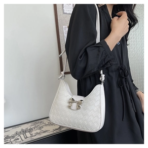 Detail of white woven crescent bag featuring a silver metal bow buckle on a black dress