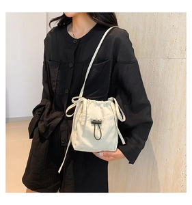 Detail of cream drawstring bucket bag showing front pocket and adjustable strap texture