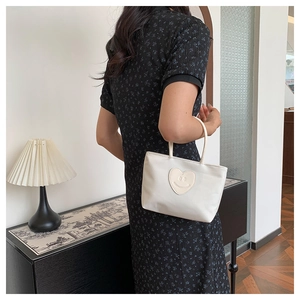 Detail of white canvas handbag with beige heart-shaped smiley face patch and slim handles