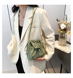 Olive green nylon bucket bag with drawstring closure shown on a female model in an ivory blazer