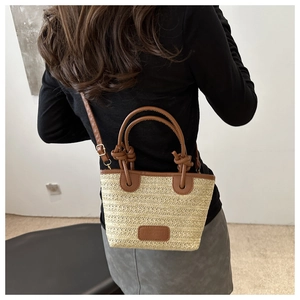 Close-up of a woven tote bag with brown leather handles and adjustable shoulder strap