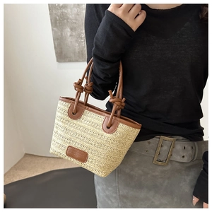 Detail of hand-woven straw tote with brown leather handles and brand logo tag