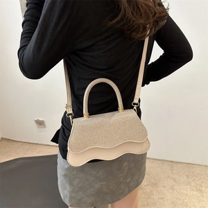 Sac bandoulière élégant avec rabat pailleté et base en cuir crème ondulé sur un modèle