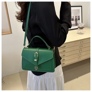 Green leather crossbody bag with gold buckle shown on model in home setting