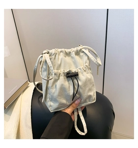 Detail view of cream nylon bucket bag featuring a drawstring closure and front mesh pocket