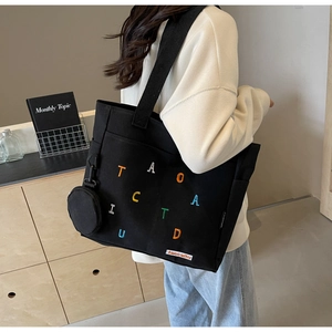 Detail of a black canvas tote bag with colorful embroidery and a small round pouch attached