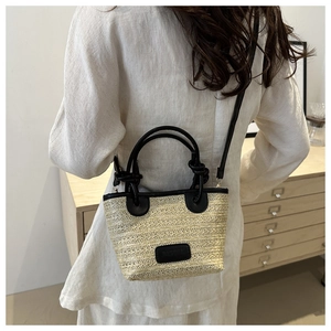 Detail shot of the woven texture and black leather handles on a natural straw tote bag