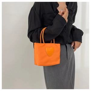 Detail of a bright orange nylon bucket bag with a heart smiley patch on casual outfit