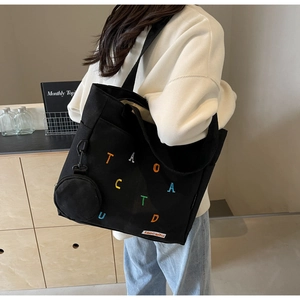 Detail of black canvas tote bag with colorful letter embroidery and small round coin purse
