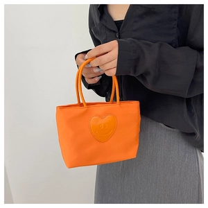 Detail of an orange nylon bucket bag with a heart-shaped smiley patch held by a model