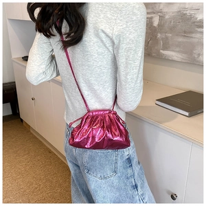 Detailed view of magenta metallic pleated pouch bag with slim shoulder strap on model