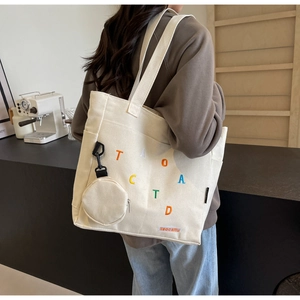 Detail of off-white canvas tote bag with colorful embroidery and matching coin purse charm