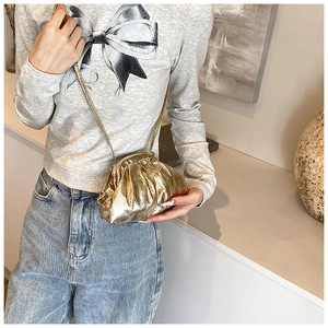 Detailed view of a metallic gold pleated mini shell bag worn on a casual crossbody strap