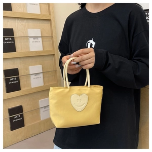 Detail of yellow nylon bucket bag featuring a minimalist heart smiley patch and woven handle