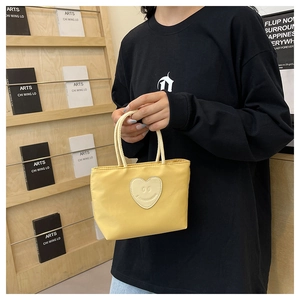 Detail of yellow nylon handbag with heart smile patch held by model in casual setting