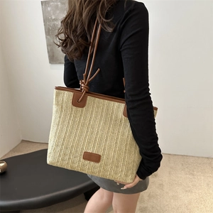 Straw tote bag with brown leather trim and shoulder straps worn by model in minimalist room