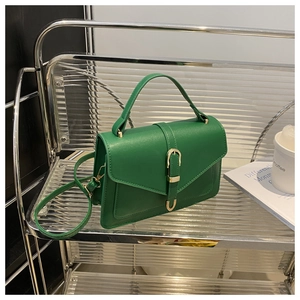 Detail of dark green leather handbag featuring elegant gold metal clasp on a glass shelf