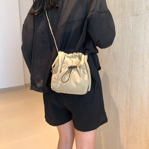 Khaki drawstring bucket bag shown on model featuring a minimalist sporty crossbody design