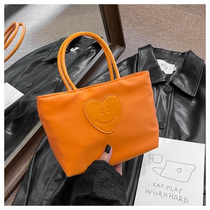 Detail view of a bright orange nylon bucket bag with a heart-shaped smiley face patch