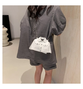 Detail of creative white jacket-shaped crossbody bag with silver chain strap on model