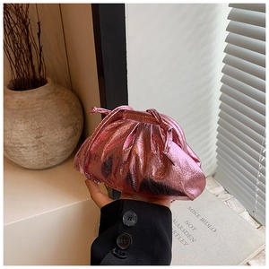 Metallic pink pleated cloud clutch bag held by hand in a sunlit interior scene