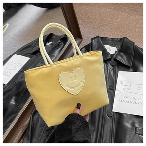 Detail of light yellow nylon bucket bag with a heart-shaped smiling face leather patch