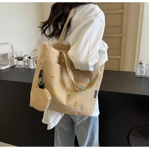 Canvas tote bag with TACTD embroidery and mini coin purse shown on a model in a cafe