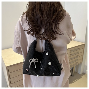Detail of black pleated hobo bag with pearl bow charms worn by a model in casual setting