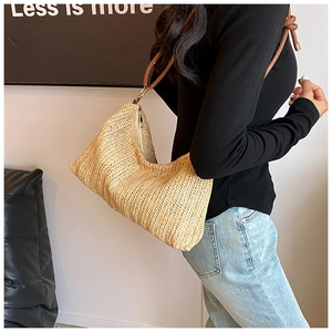 Detail of hand-woven straw hobo bag featuring brown leather strap and contrast knot detail