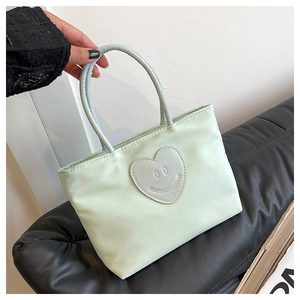 Detail of mint green nylon tote bag featuring a heart-shaped smiley face patch