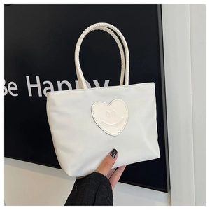 Detail of white minimalist bucket bag featuring a smiley face heart patch and round handles