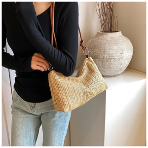 Detail of straw woven bag featuring brown leather straps and gold metal ring hardware