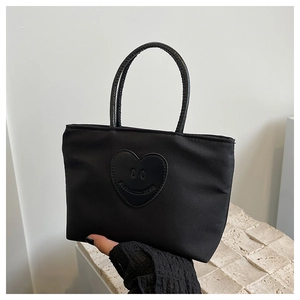 Detail of black nylon bucket bag featuring a leather heart patch and smiling face logo