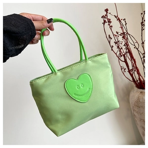 Close-up of light green bucket bag with heart emoji patch and satin fabric texture