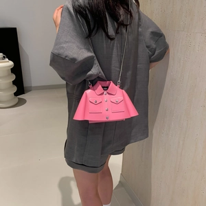 Pink jacket-shaped crossbody bag with silver chain strap worn by model in minimalist setting