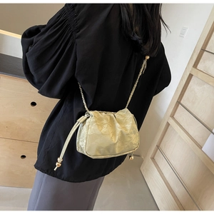 Close-up of a creamy yellow ruched crossbody bag with gold chain strap detail
