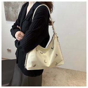 Detail of cream tote bag with silver butterfly metal charms and chain strap on model